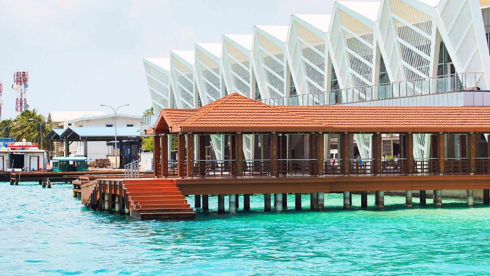 Male International Airport pier in Maldives with turquoise water sea and white building in background.