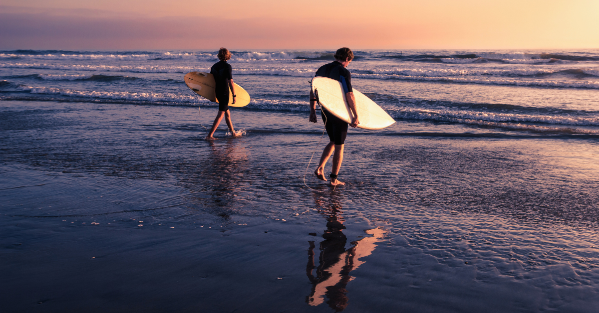 two people surfing in Oahu during sunset