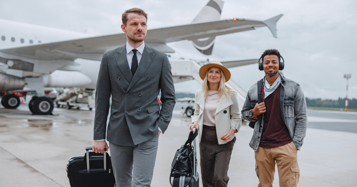 Smiling woman wearing a hat,  man wearing a suit, andman wearing headphones boarding a private aircraft at the airport