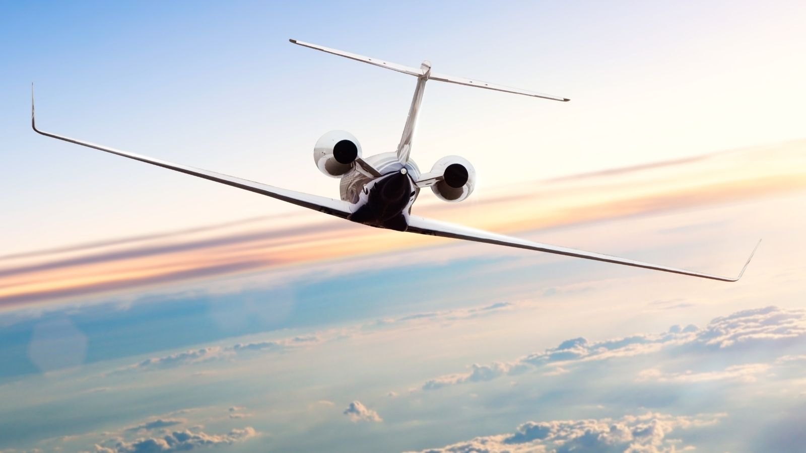 A white private jet in flight against a blue sky with white clouds